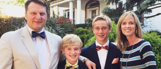 a smiling family dressed formally posing in front of their home